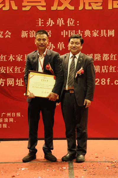 中国传统家具研究会秘书长高肃(右)为横店红木家具中心董事长张志权(左)颁奖