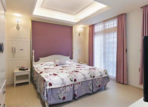 延续客厅以简单线板营造新古典质感的手法，再以粉紫色漆面床头墙跳出空间重点，与浅木色地坪搭构温馨氛围